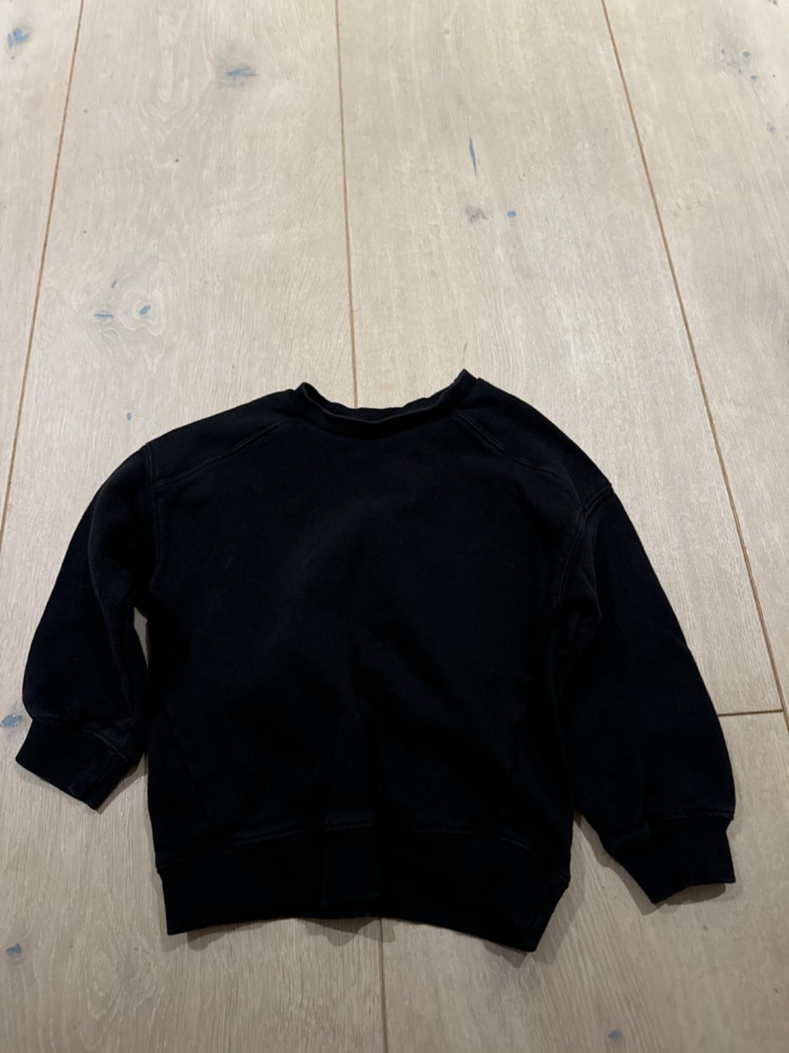 Black long-sleeved sweatshirt on a light wooden floor, viewed from above.