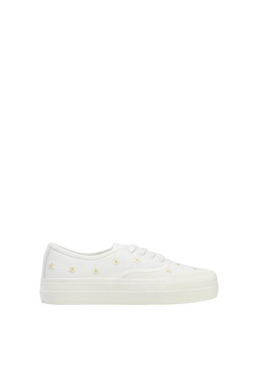 White platform sneaker with embroidered small yellow flower details on a white background.