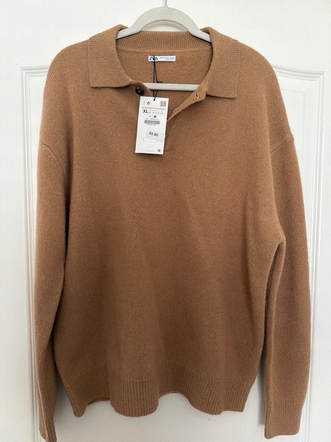 Brown collared sweater with a hang tag showing size XL and price 69.90, hanging on a white hanger in front of a white door.