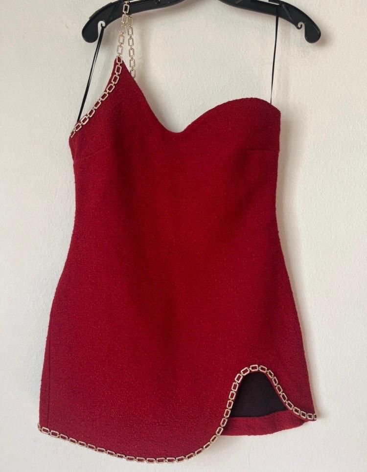Red strapless dress with chain detail on the hem and strap, hanging on a black hanger against a white background.