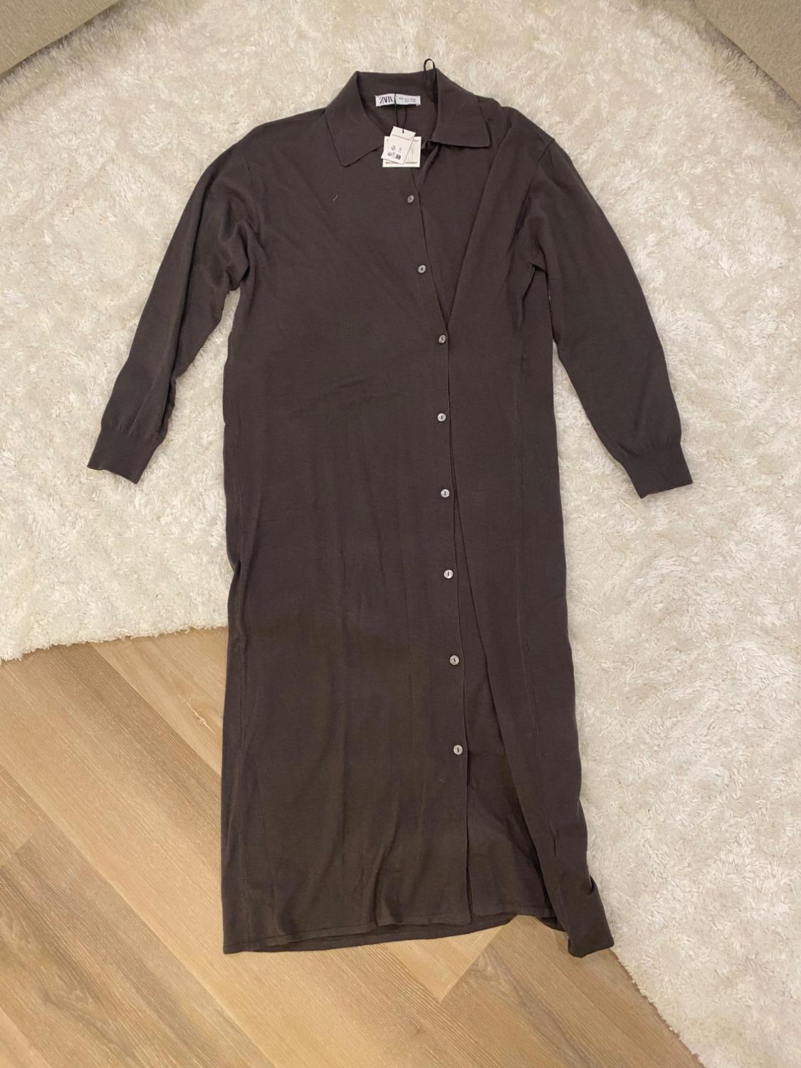 Brown long-sleeved dress with buttons, on a white rug and wooden floor. Visible tag on the collar.