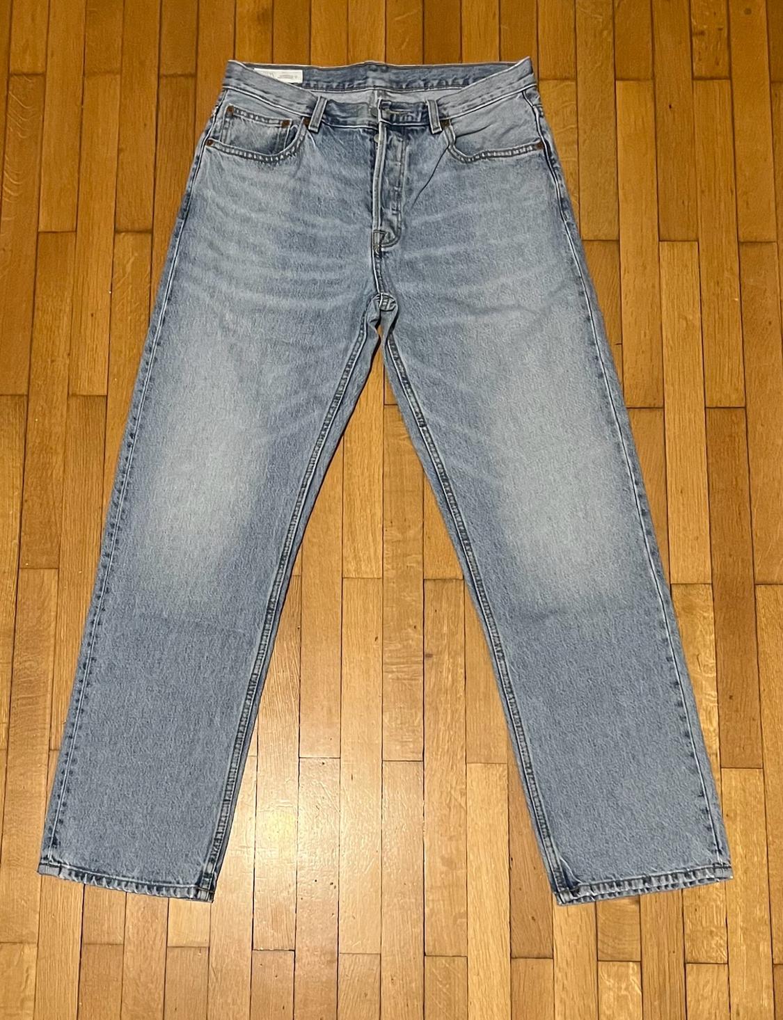 Light blue straight-cut denim jeans, laid out on a wooden slatted floor. Casual and relaxed style.
