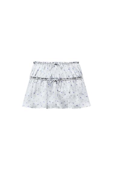 White miniskirt with blue floral print, tiered design, and adjustable ties on a white background.