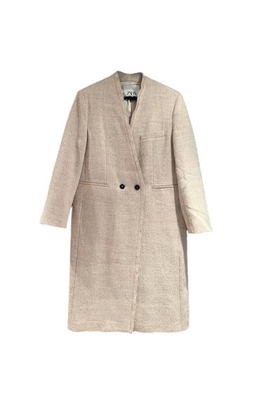 Long beige coat with double-breasted fastening and front pockets. Visible label on the collar. White background.