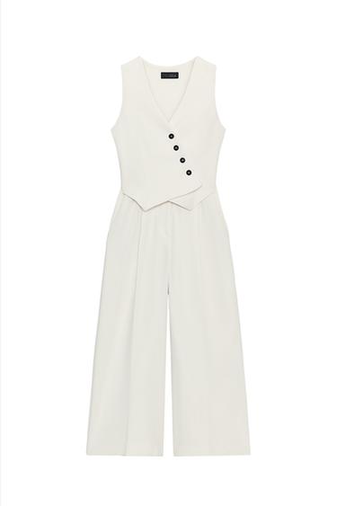 Front view of a raw denim jumpsuit with a V-neck, cross-over buttons, front pockets, and wide legs with pleats.