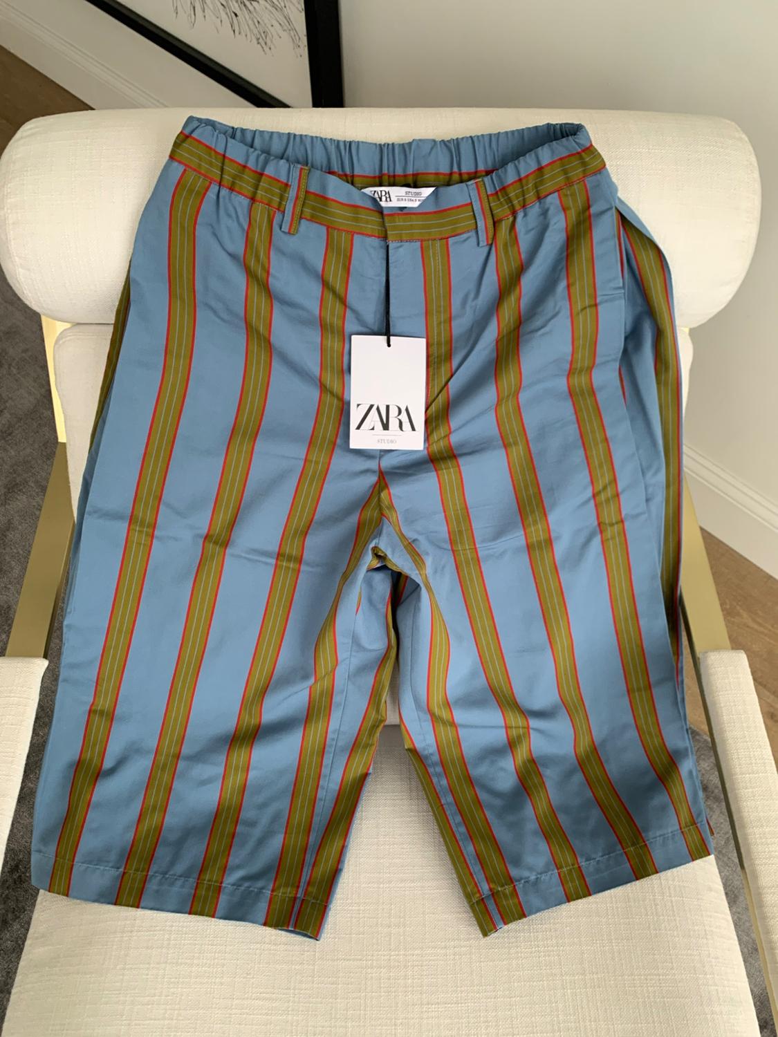 Blue shorts with vertical green and red stripes on a white chair. Visible label bearing the text ZARA STUDIO.