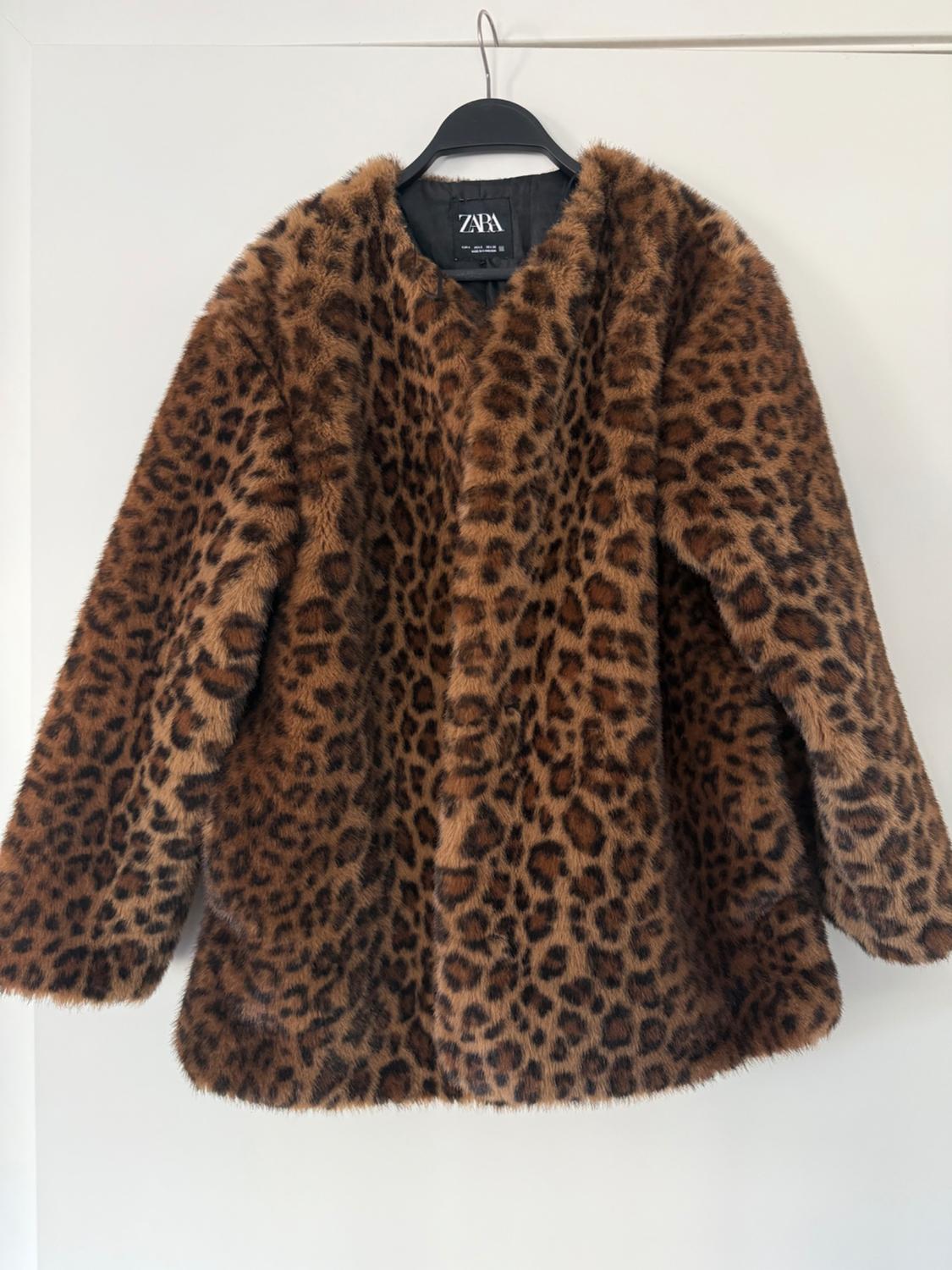 Faux fur leopard print coat hanging on a black hanger. Visible tag: ZARA. White background.