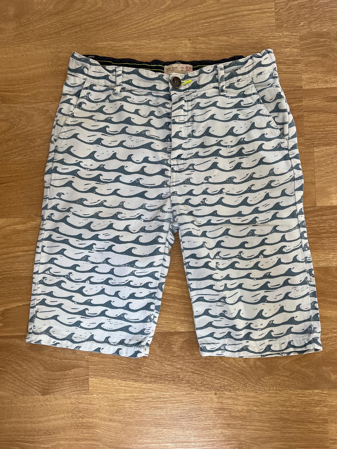 Blue wave print shorts on a white background, placed on a light wooden floor.