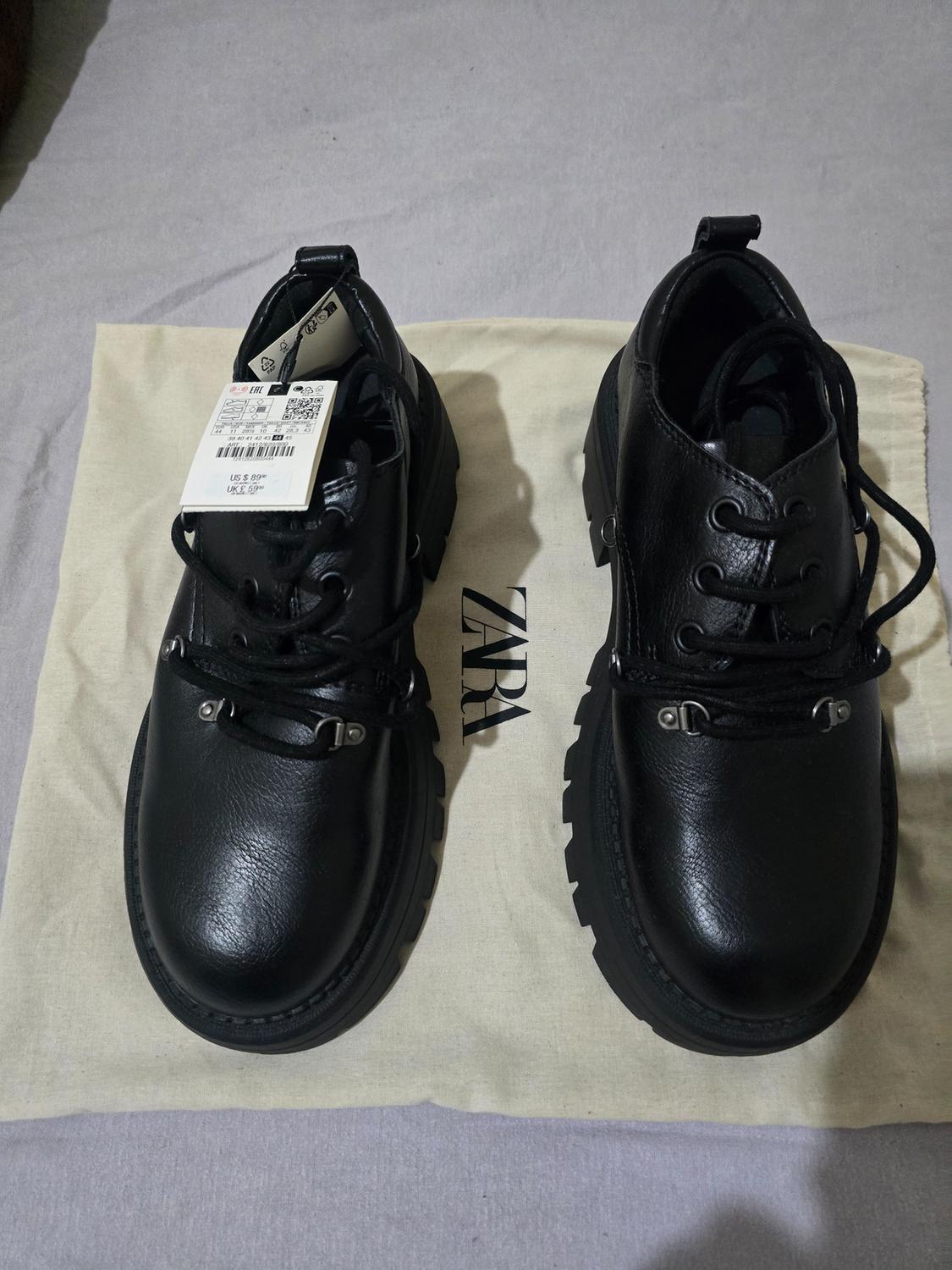 Pair of black lace-up shoes with a ridged sole on a canvas bag bearing the text ZARA.