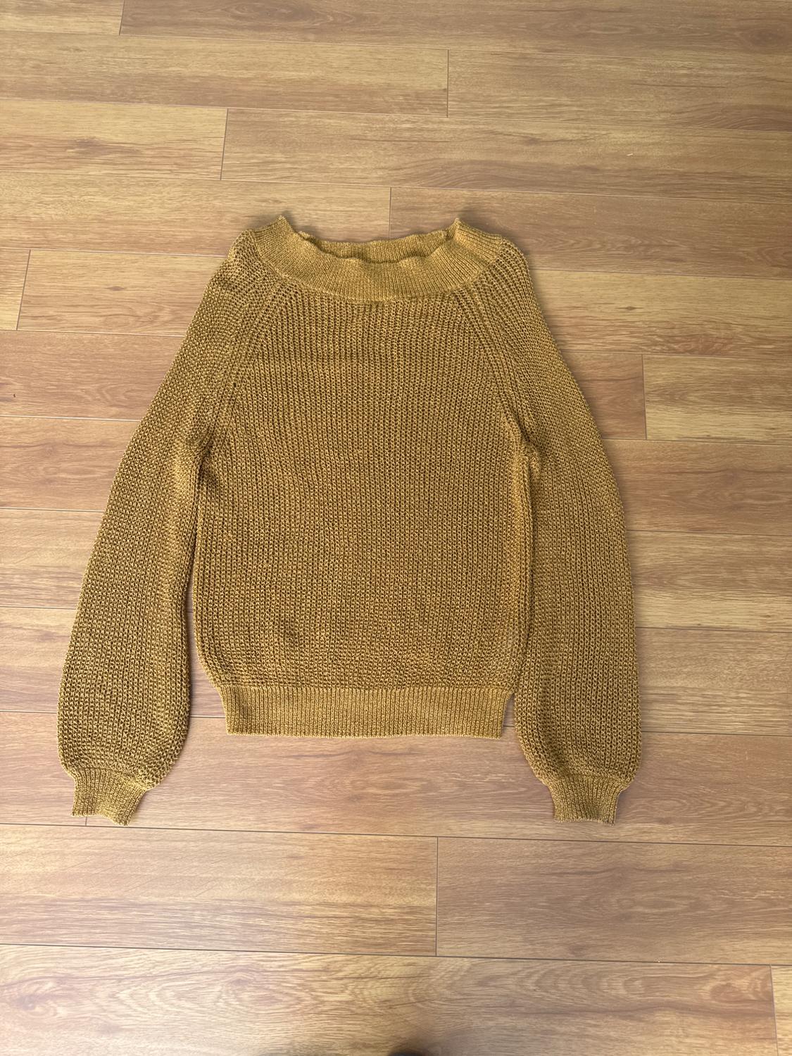 Mustard knit jumper on a light wooden floor. Long-sleeved design with a round neck and chunky texture.