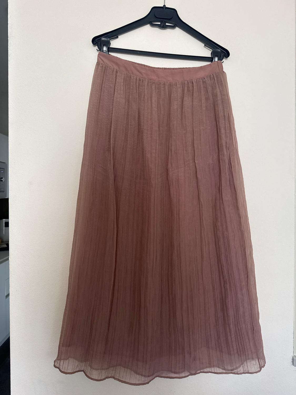 Old rose pleated maxi skirt hanging on a black hanger against a white wall.