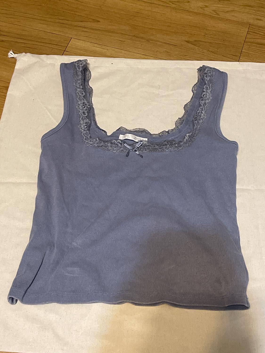 Blue tank top with lace at the neckline, on white fabric and wooden floor.