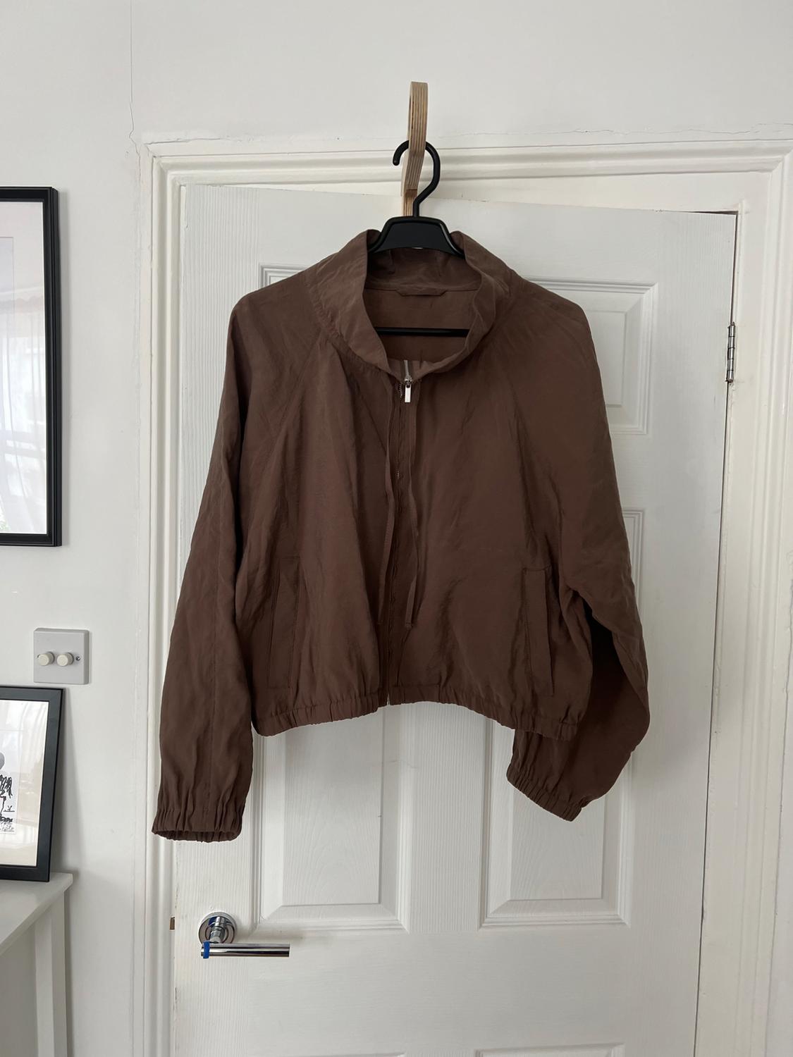 Brown zipped jacket hanging from a coat hanger on a white door. Casual style in a relaxed indoor setting.