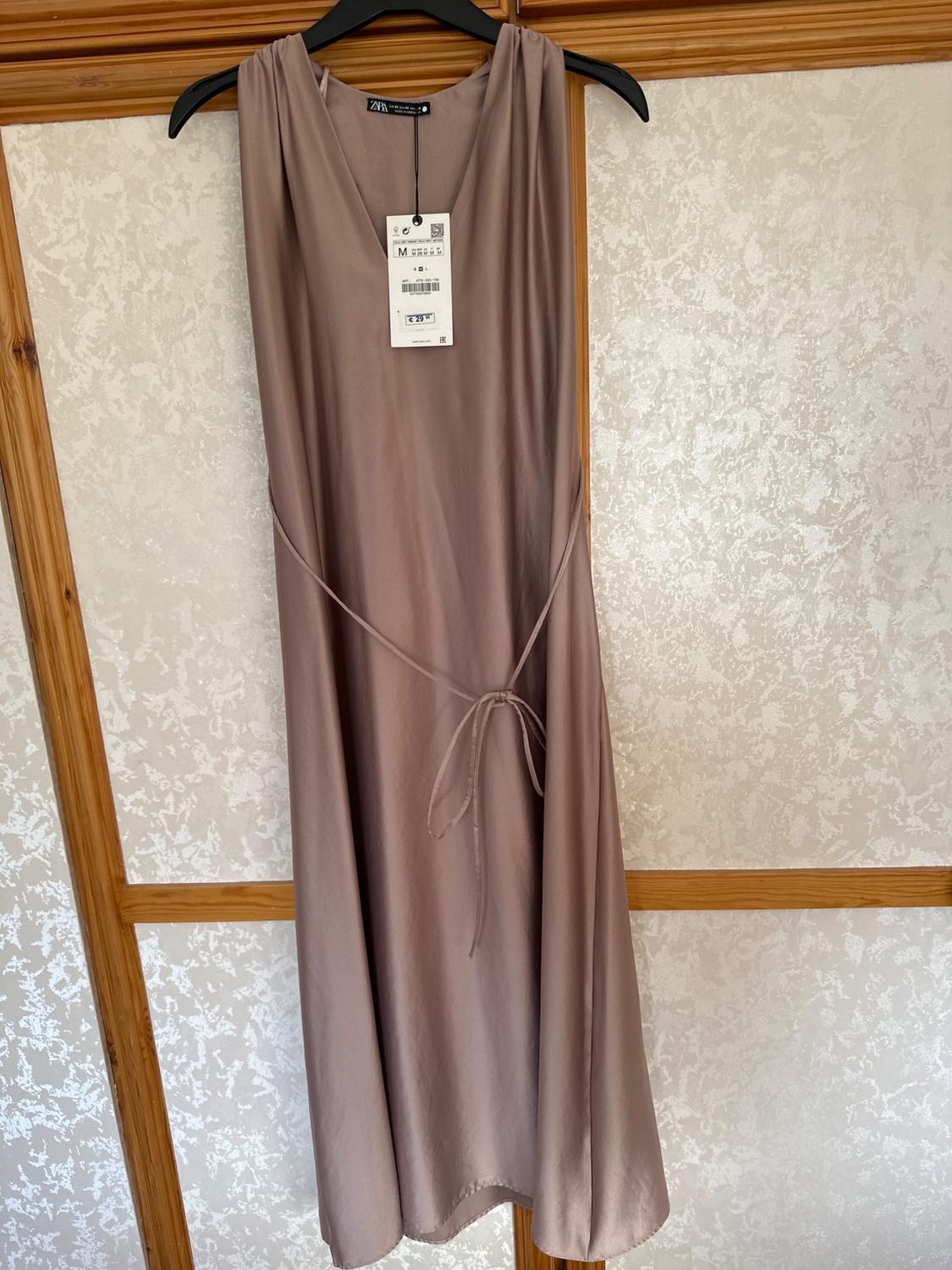 Front view of sleeveless beige dress with adjustable belt and visible label on the chest.