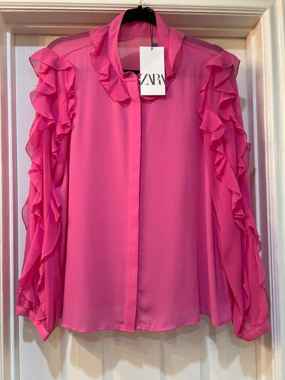 Pink blouse with ruffles on the sleeves and collar, hanging on a hanger. Visible tag with the text "ZARA".