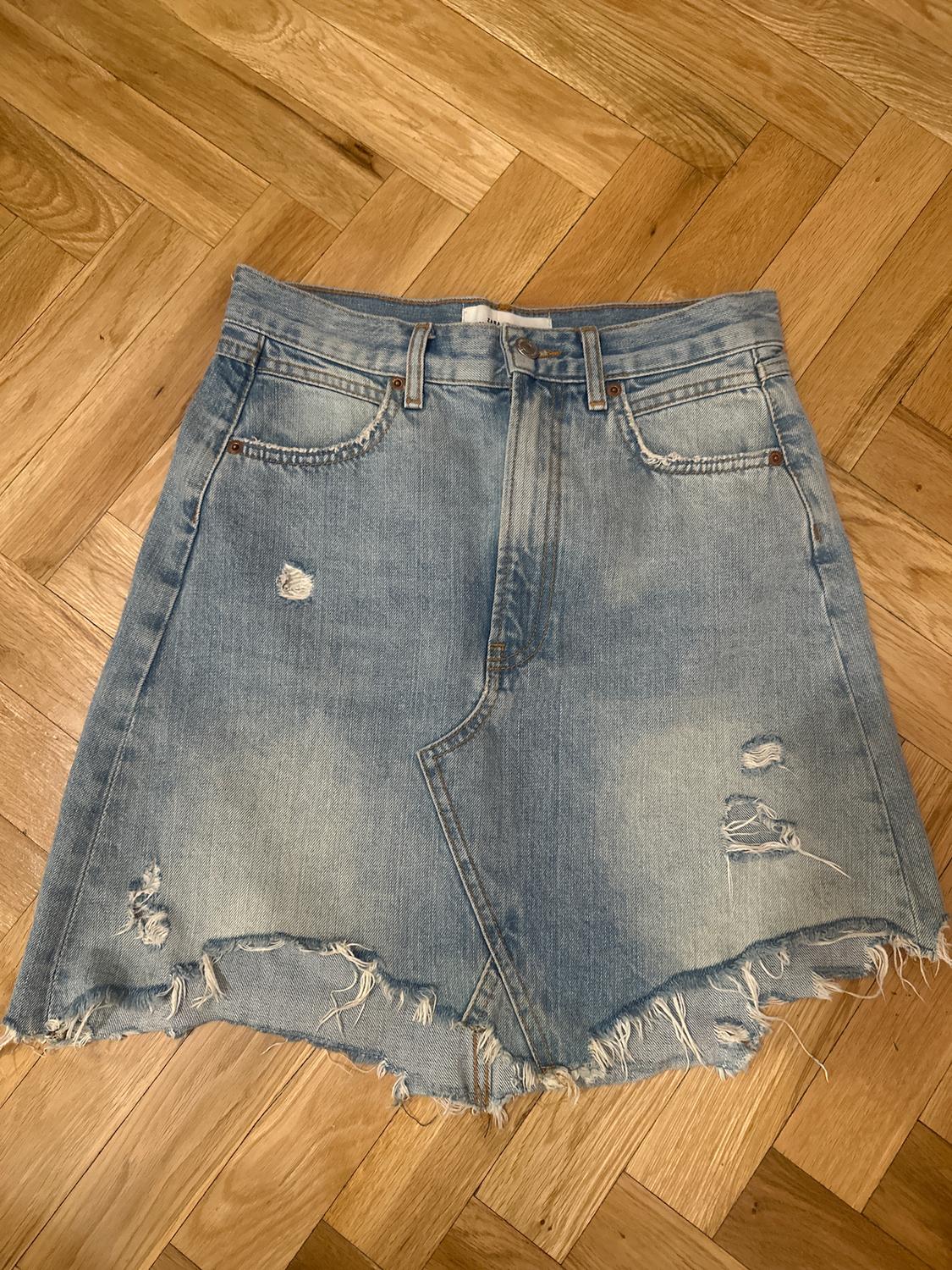 Distressed blue denim skirt with rips and a frayed hem, on a light herringbone wooden floor.