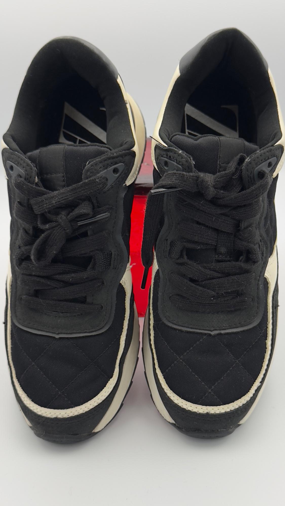 Black sneakers with white details, top view. White background with a touch of red in the center. Black shoelaces.