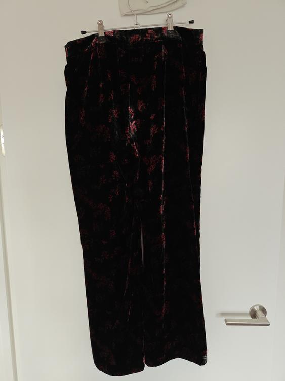 Black velvet trousers with a red floral print, hanging on a white door with a metal hanger.