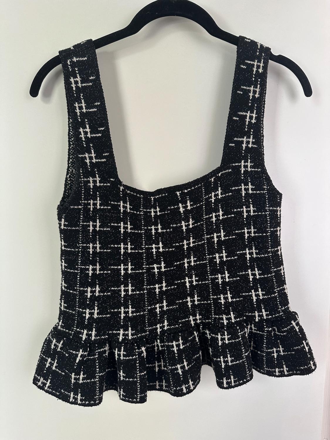 Black knitted camisole top with a white check pattern and a frilled hem, hanging on a black hanger against a white background.