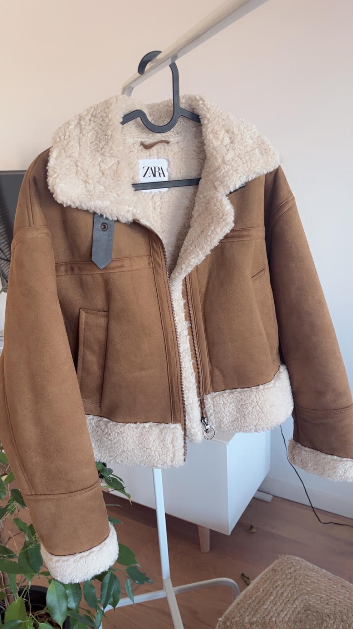 Brown jacket with white fleece lining, hanging on a black hanger. Visible label with the text "ZARA". Light interior background.