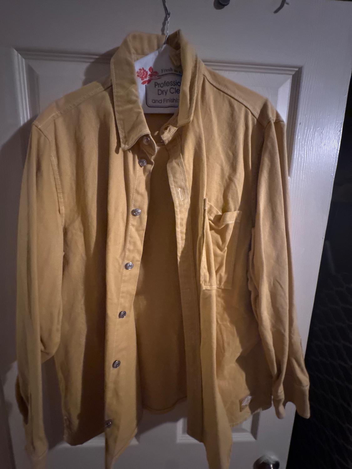 Yellow shirt hanging on a white door, with silver buttons and a visible label that reads "Professional Dry Clean and Finishing".