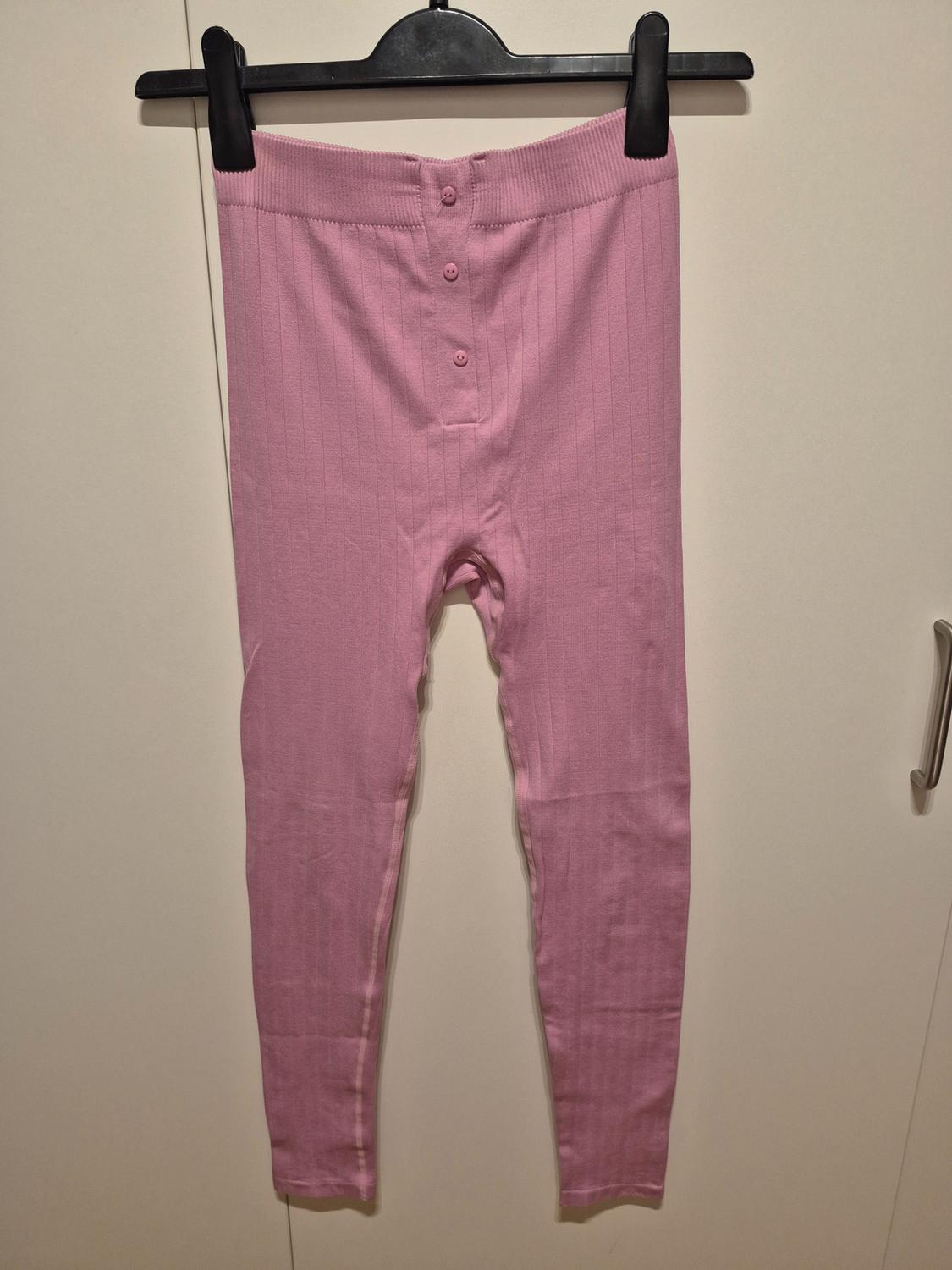 Light pink long trousers with buttons at the waist, hanging on a black hanger against a white background.