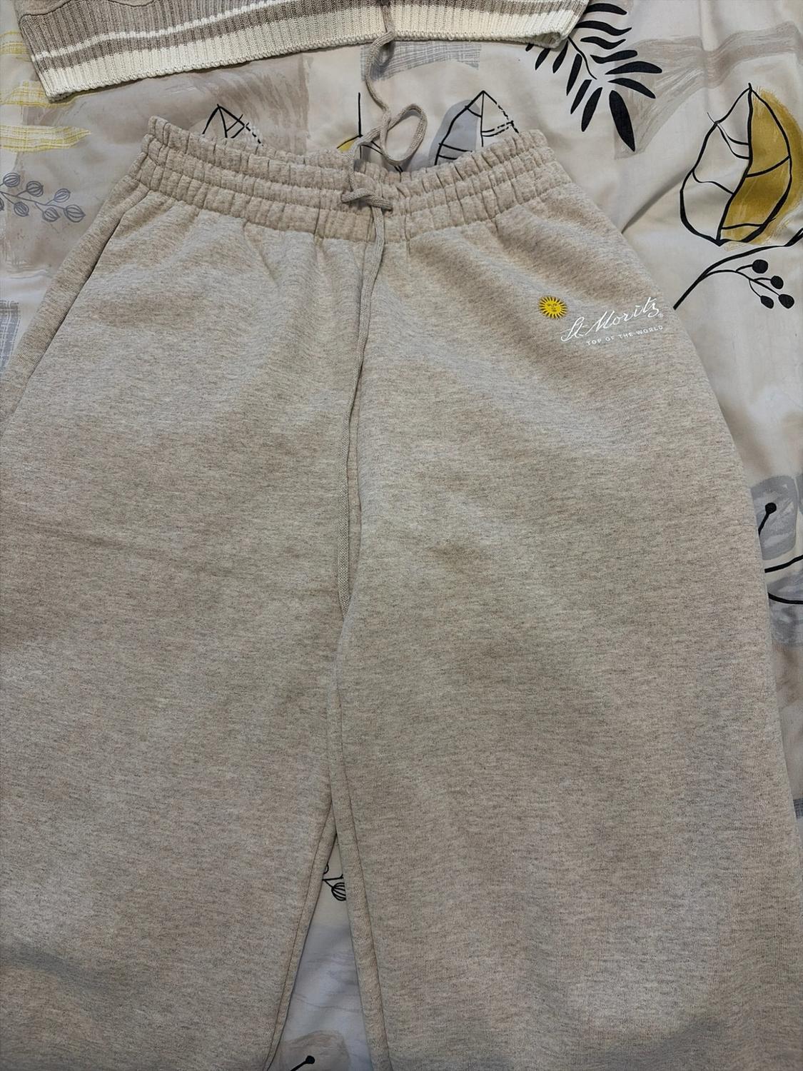 Light grey trousers with an elasticated waist on a patterned sheet.
Includes the text "St. Moritz TOP OF THE WORLD" and a yellow sun.