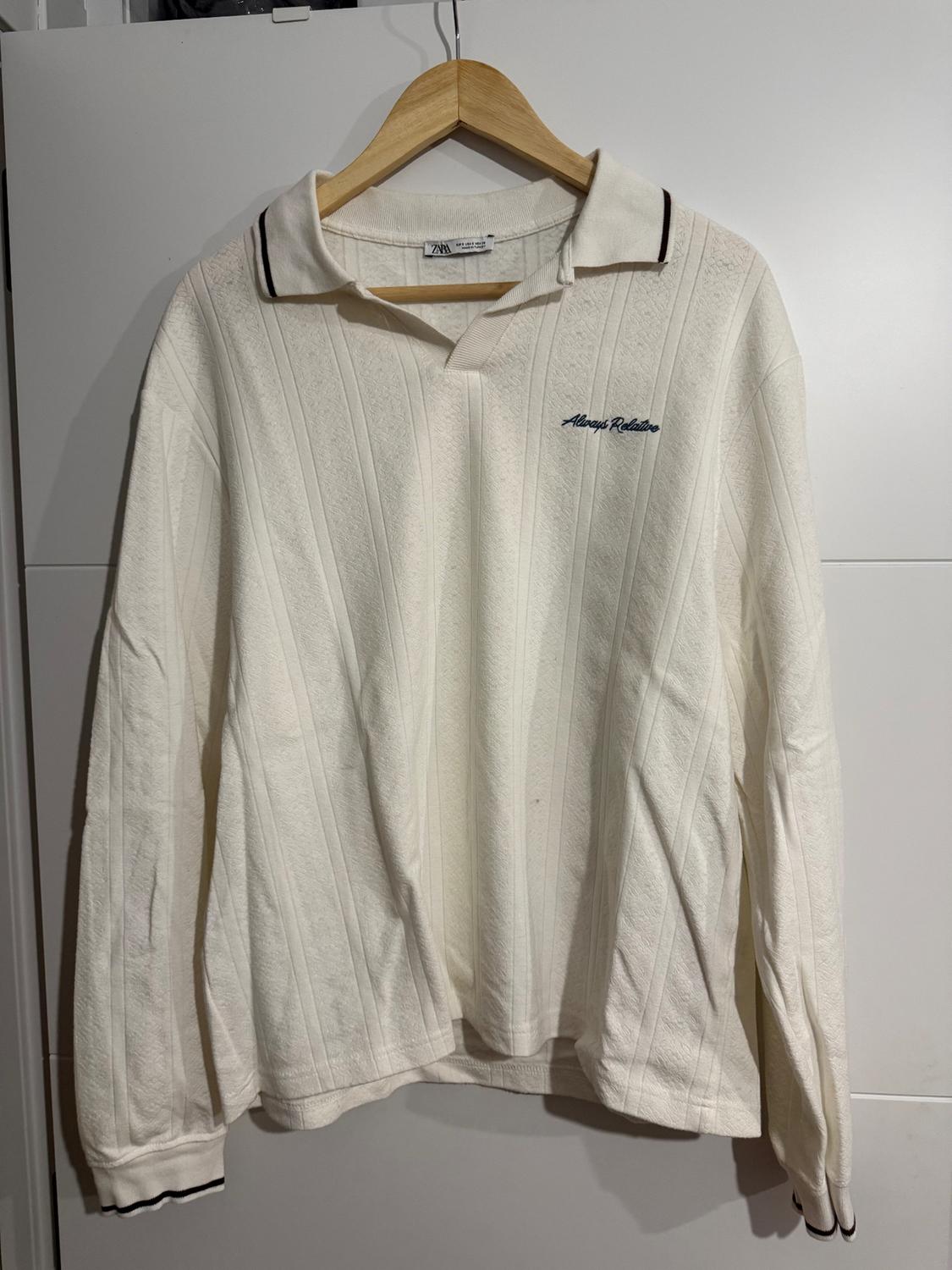 White long-sleeved polo shirt with vertical stripe texture, hanging on a wooden hanger. Visible text: "Always Relaxing".