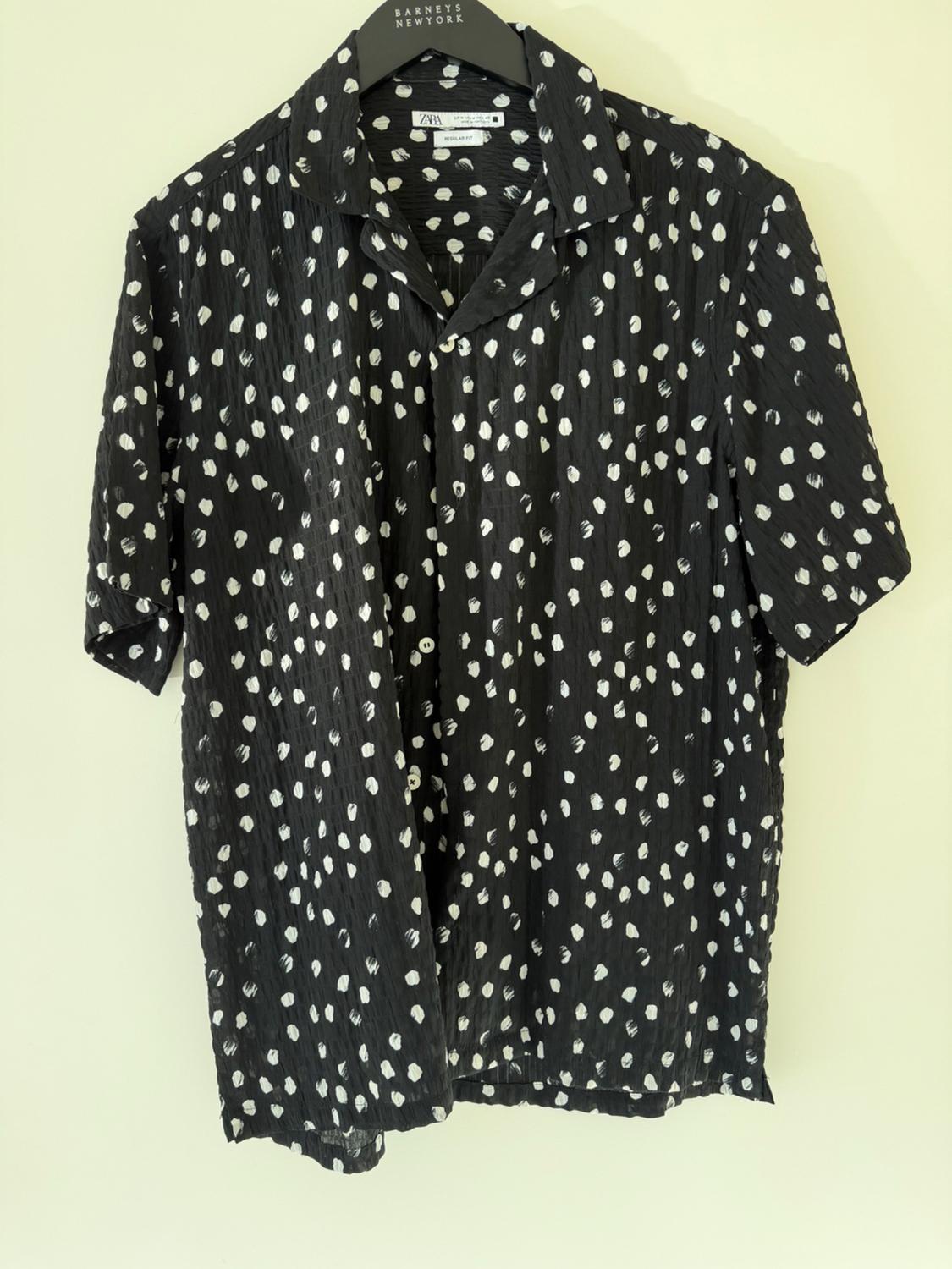 Short-sleeved black shirt with irregular white polka dots, on a hanger against a light background. Text: BARNEYS NEWYORK ZARA REGULAR FIT.