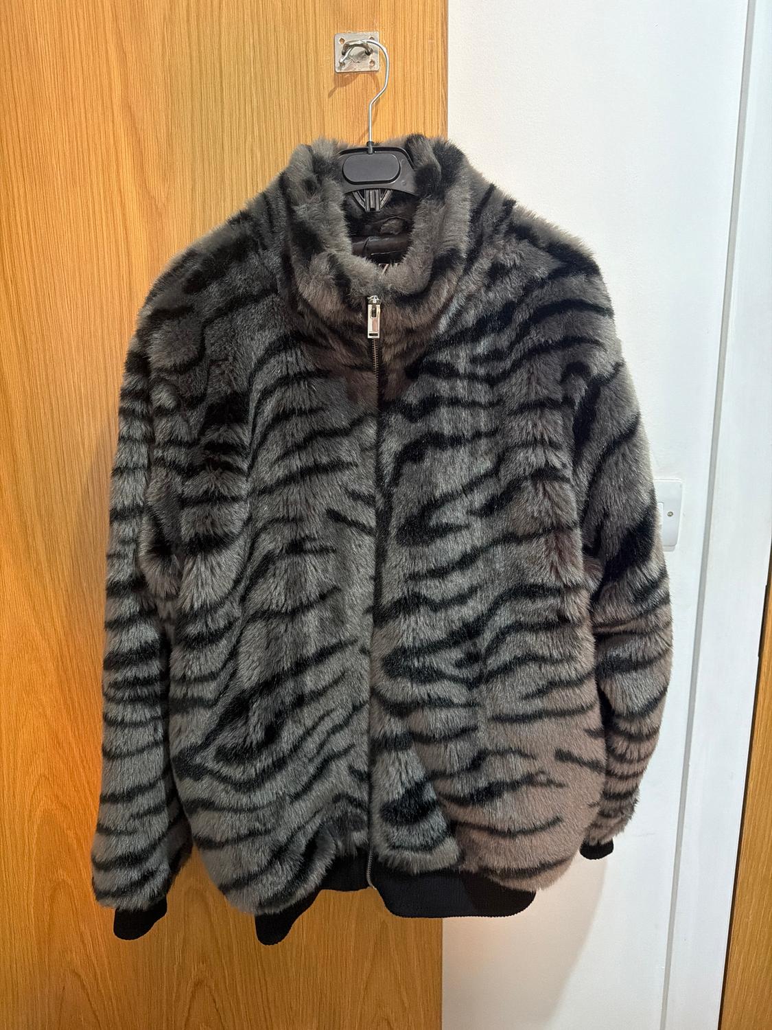 Faux fur jacket with black and grey striped print, hanging on a hanger over a wooden door.