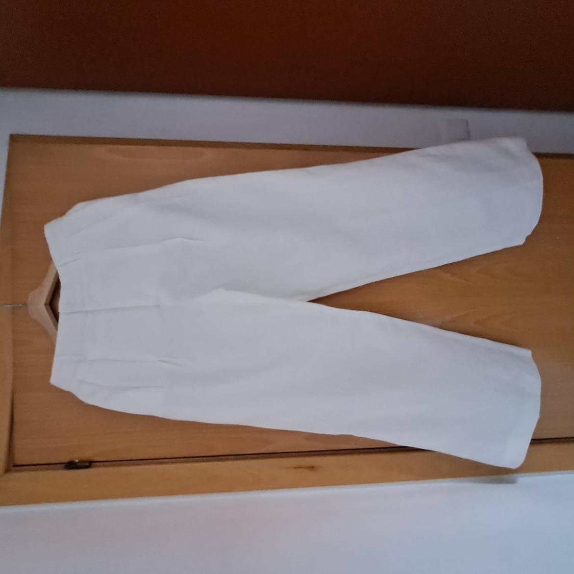 Wide white trousers with pleats on a wooden surface with a hanger. Casual and relaxed style in a flat lay composition.