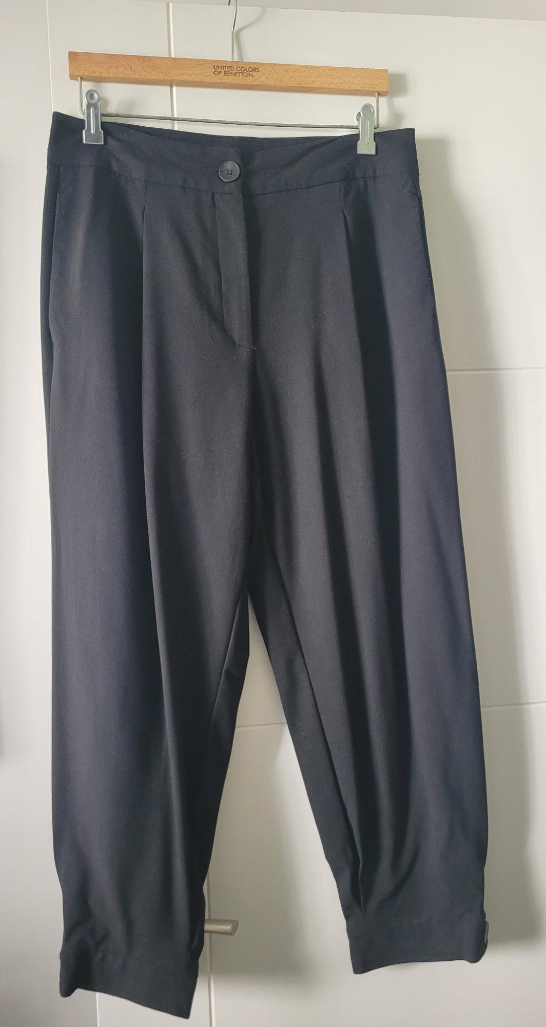 Black trousers hanging on a wooden hanger with the text "United Colors of Benetton" on a white background.