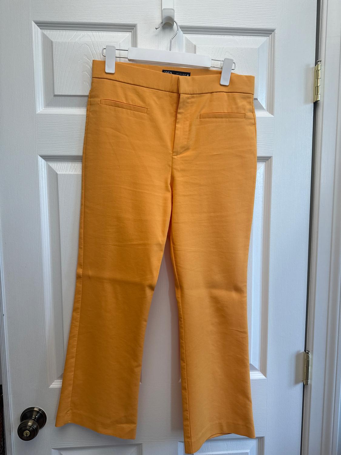 Yellow trousers hanging on a white hanger over a white door. Front pockets visible.