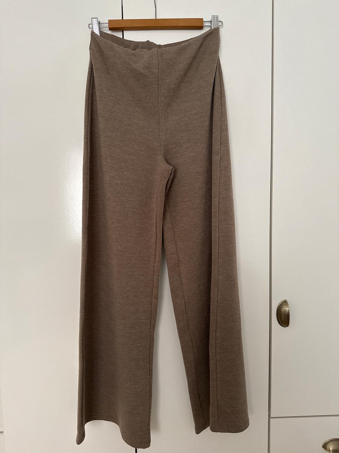 Brown wide-leg trousers hanging on a wooden hanger in front of a white wardrobe.