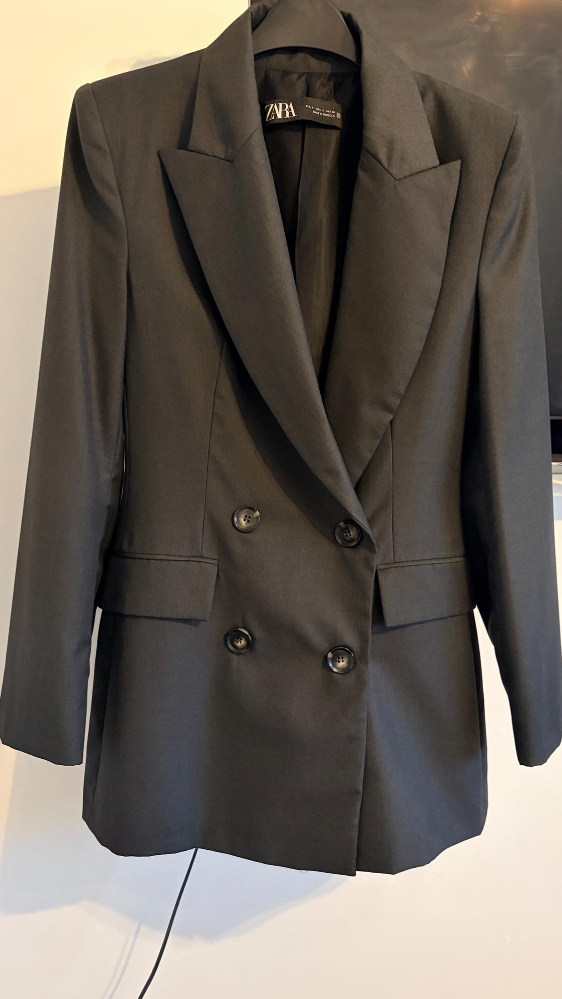 Black double-breasted jacket hanging on a hanger. Visible label with the ZARA brand on the inside of the collar.