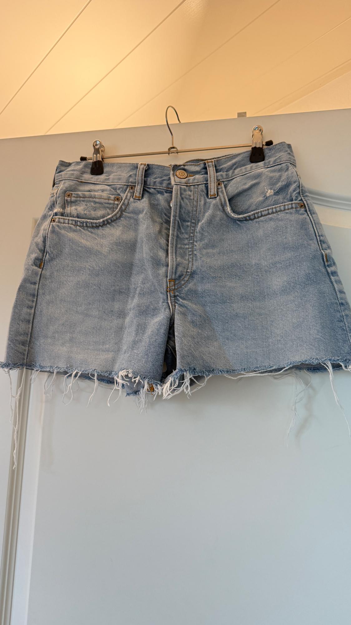 Light blue denim shorts with a frayed hem hanging on a hanger over a white door.