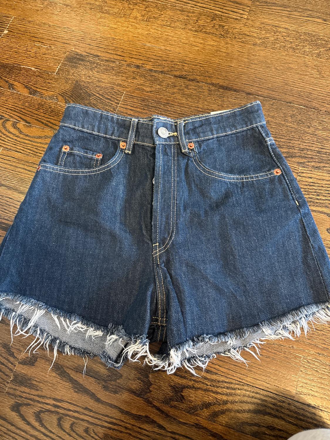 Blue denim shorts with frayed hem, on a brown wooden floor.