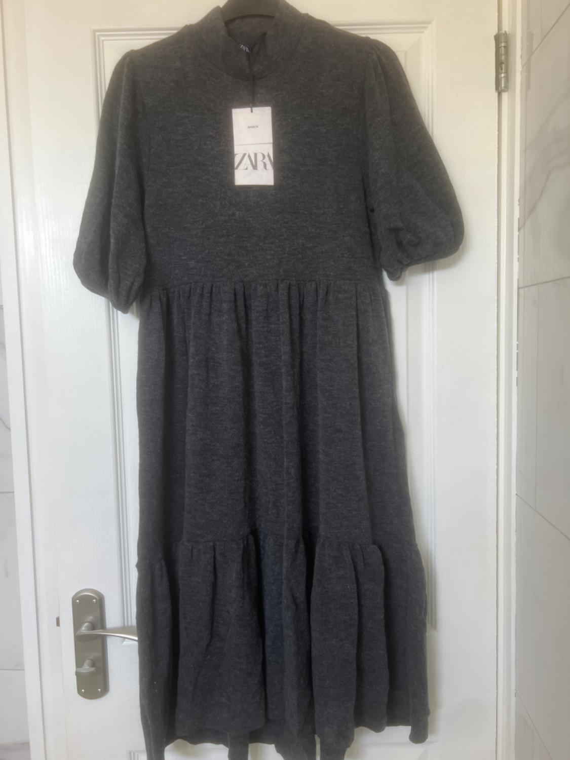 Dark grey short-sleeved dress hanging on a white door. Visible label with the text "ZARA".