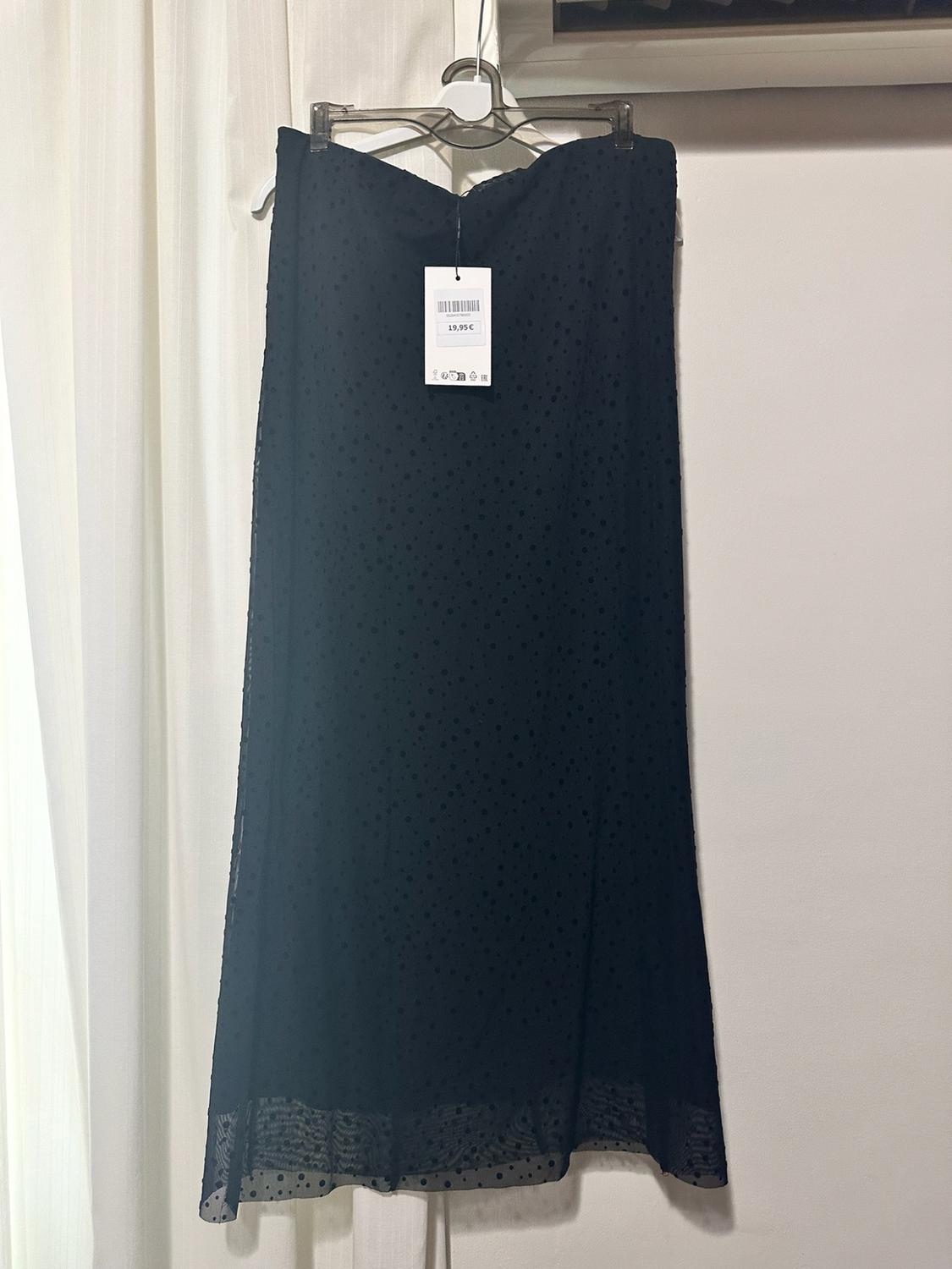 Black long polka-dot skirt with a semi-transparent hem hanging on a white wall. Label displaying the text €19.95.