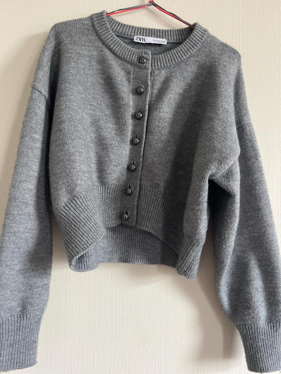 Gray knit cardigan with long sleeves, dark front buttons, a crew neck, and ribbed edges. The ZARA brand label is visible on the collar.
