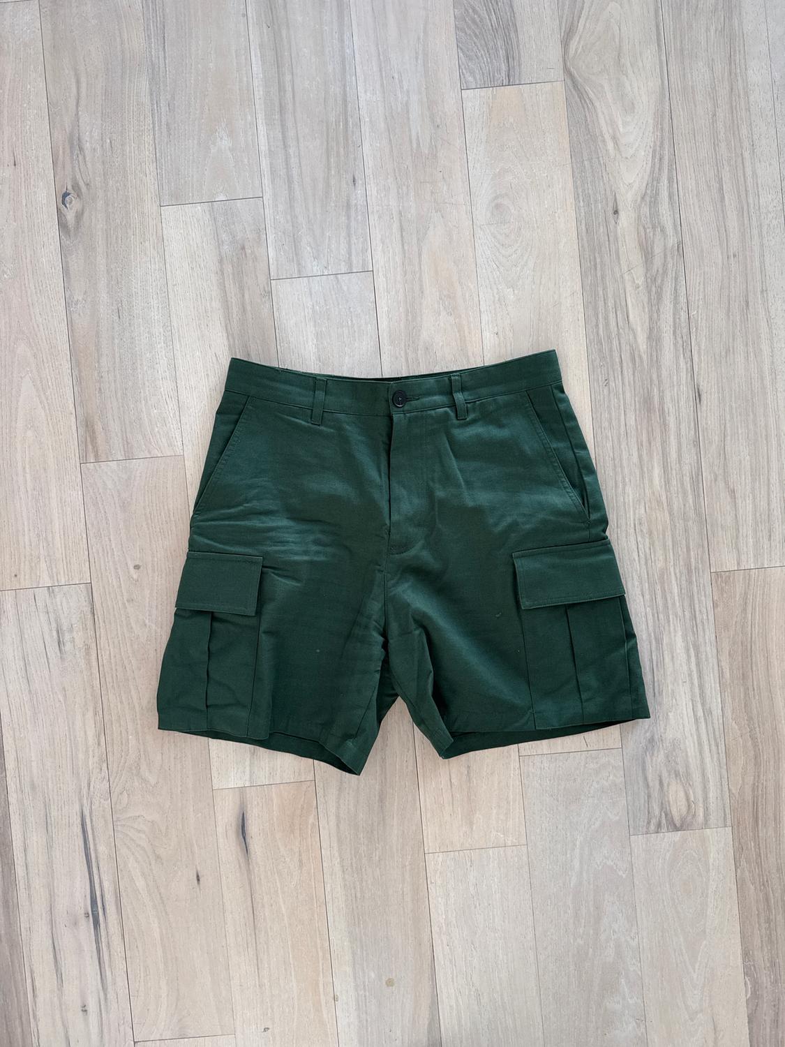 Dark green shorts with large side pockets, laid on a light wooden floor.