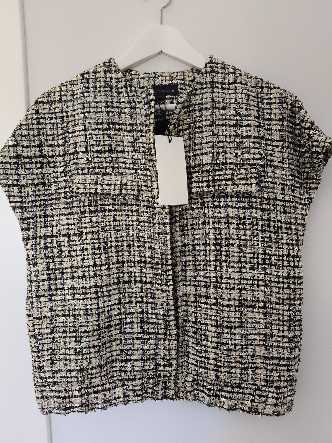 Black and white textured fabric jacket hanging on a white hanger, with visible swing tag.