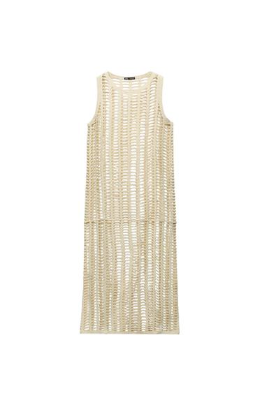 Sleeveless open-knit dress in beige, hanging against a white background. Visible label at the neck.