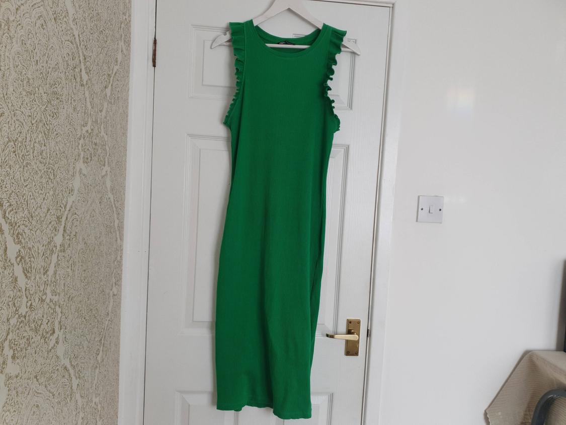 Sleeveless green dress with ruffles hanging on a white door, in a relaxed home setting with wallpaper.