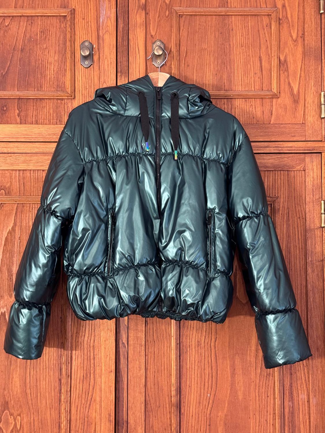 Dark green padded jacket with a hood and black drawstrings, hanging on a panelled wooden door.