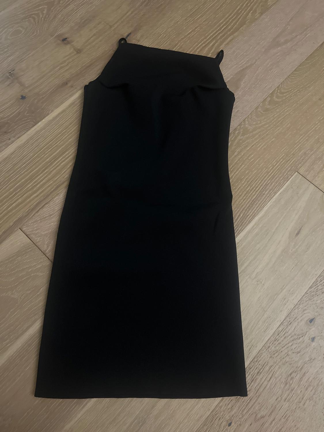 Sleeveless black dress on light wood flooring, with thin straps and a simple design.