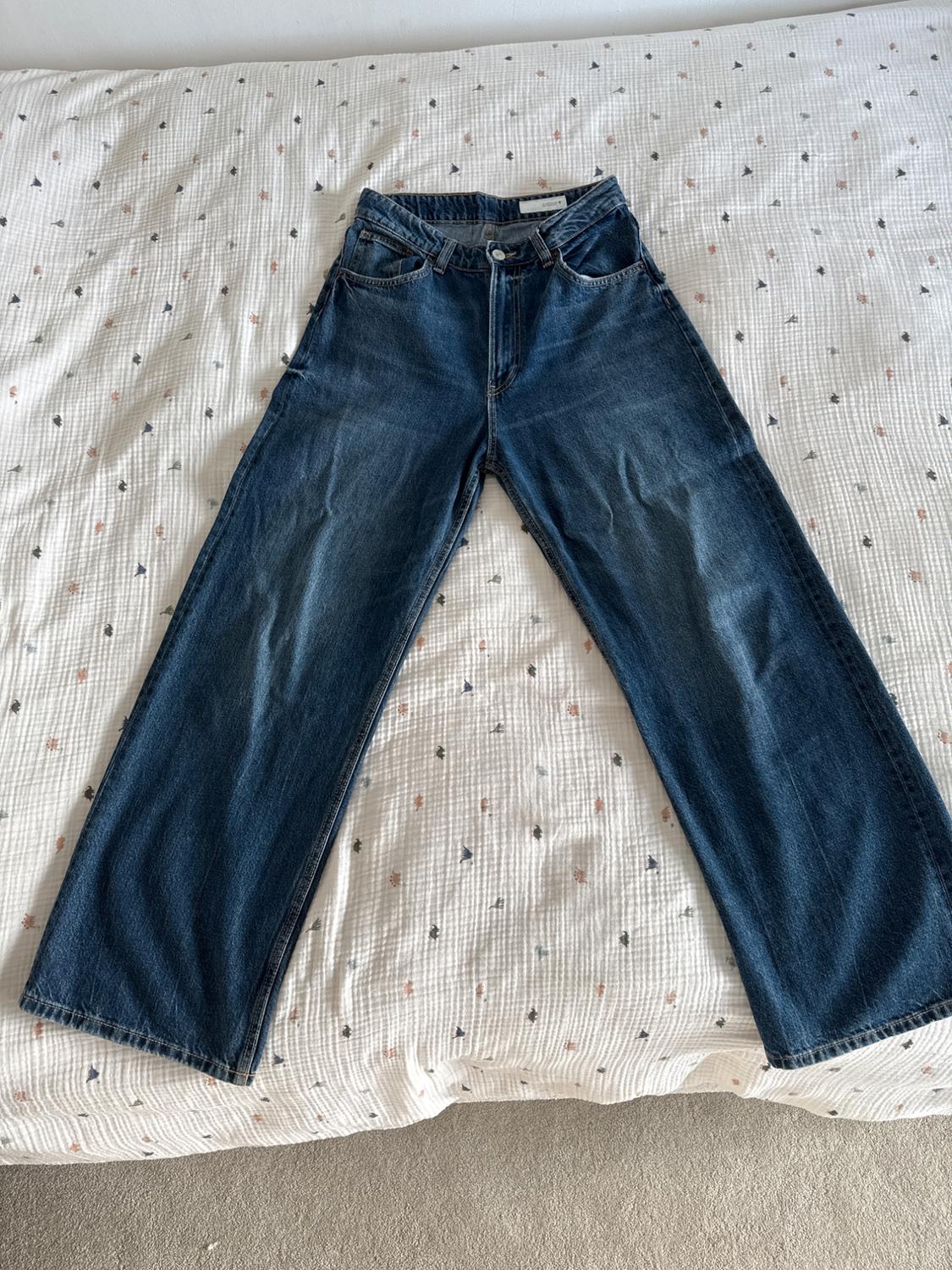 Blue wide-leg jeans placed on a white bedspread with small colourful patterns.