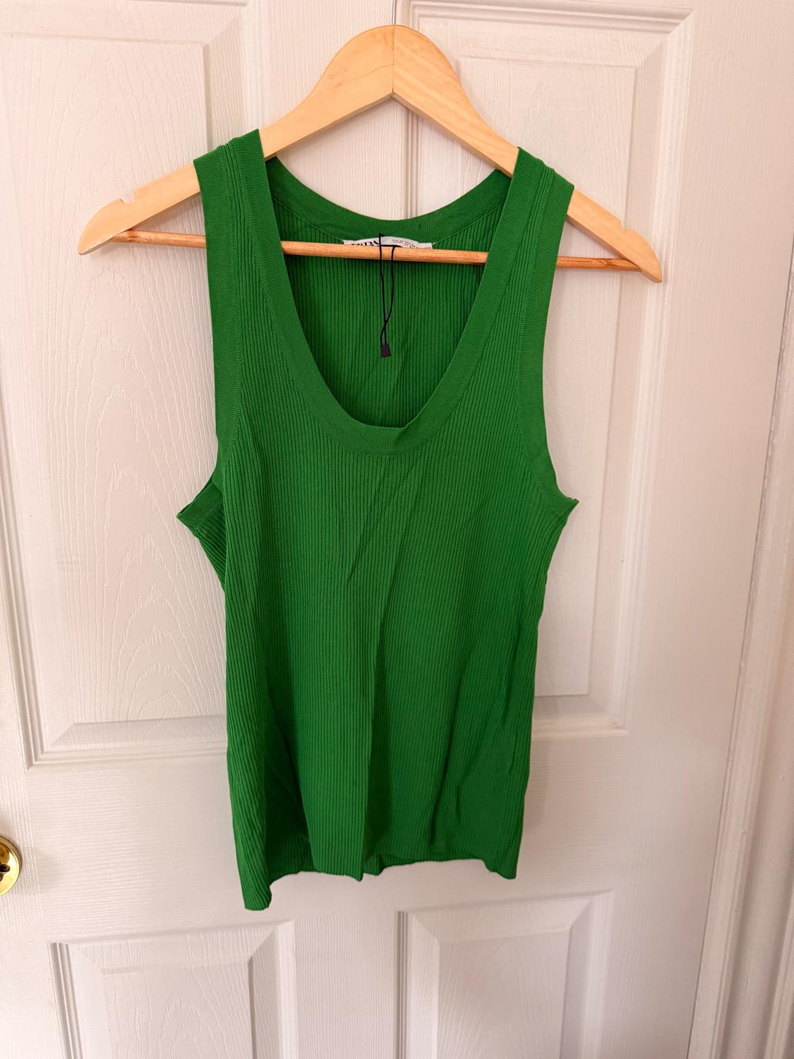 Green sleeveless shirt hanging on a wooden hanger over a white door. Ribbed texture fabric.