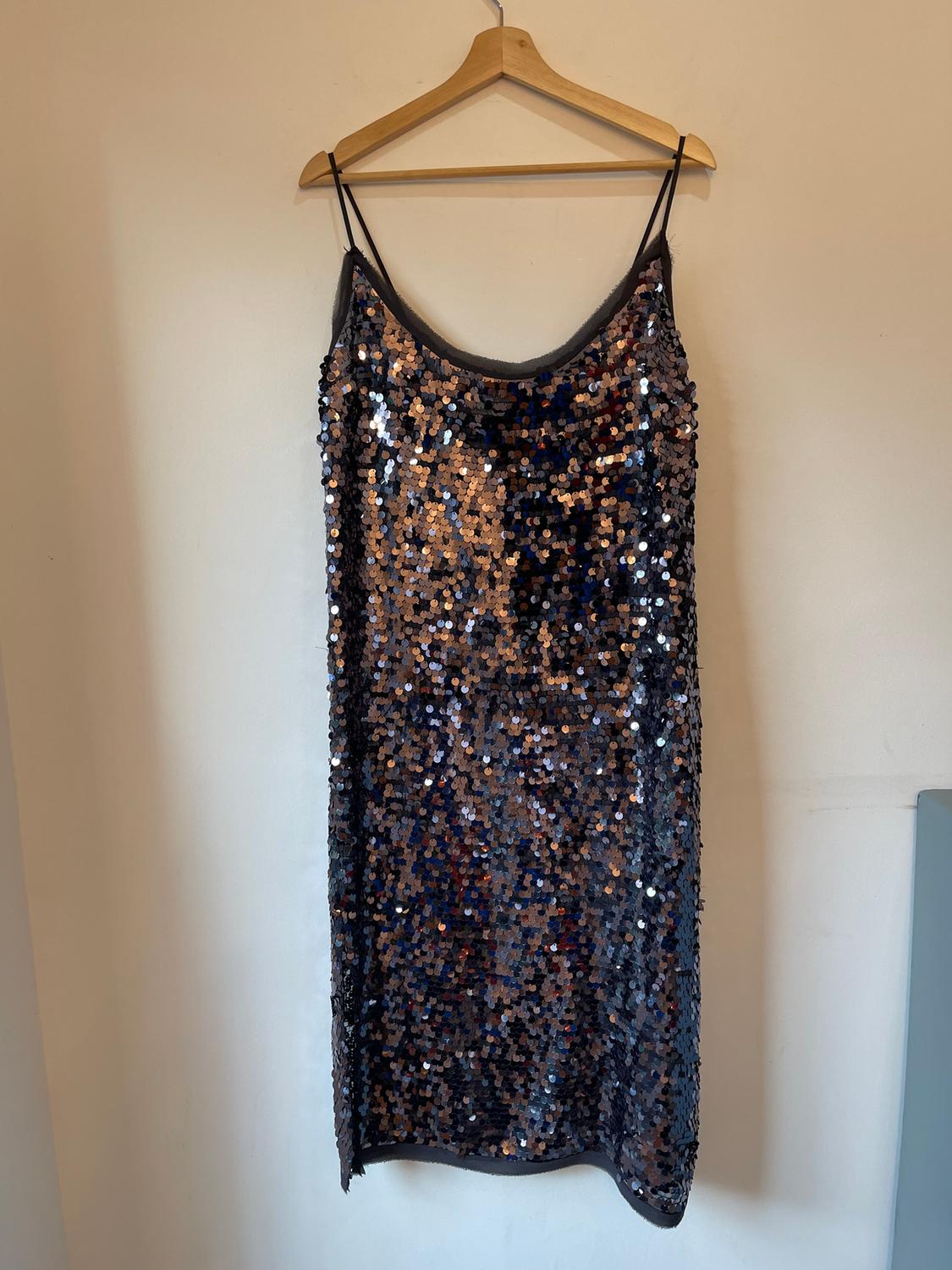 Black and gold sequined dress hanging on a wooden hanger against a white wall.