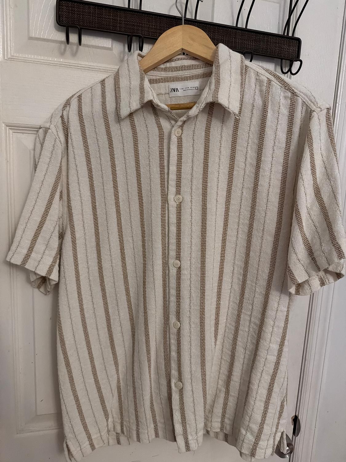 Beige and white striped shirt hanging on a wooden hanger in front of a white door.